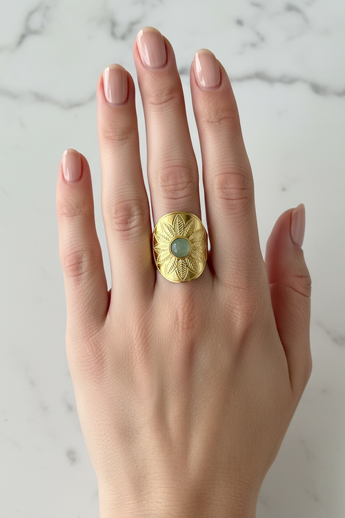 Bague dorée avec motif de feuilles et pierre verte portée sur une main élégante